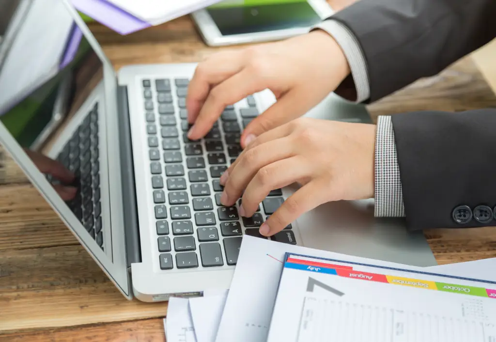 An accountant typing on a laptop beside printed ledgers and invoices